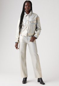 Completo in denim metallico argentato, composto da giacca e pantaloni con una vestibilità comoda, caratterizzato da tasche laterali e cuciture visibili, abbinato a stivali neri alla caviglia.
