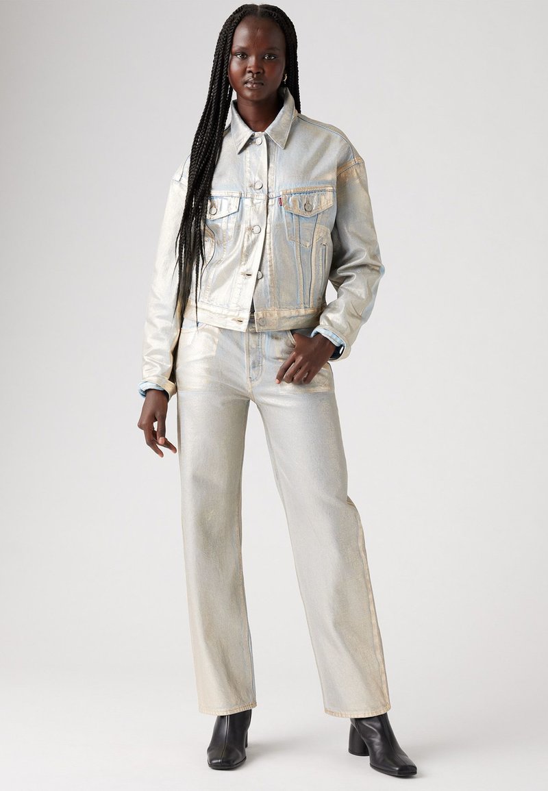 Ensemble en jean argenté métallique comprenant une veste et un pantalon à coupe décontractée, avec des poches latérales et des coutures visibles, associé à des bottines noires à la cheville.