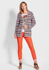 Multikleurige gebreide cardigan met strepen, van een lichte textuur. Gecombineerd met feloranje broek en bruine platform sandalen.
