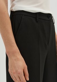 Zwarte op maat gemaakte broek met een gladde textuur, voorzien van plooien aan de voorkant, een knoopsluiting en een middelhoge taille.