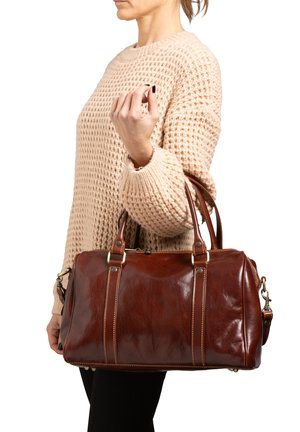 Sac à main en cuir marron avec poignées doubles, quincaillerie dorée et coutures contrastées. Le sac présente une fermeture à glissière et une forme élégante et arrondie.