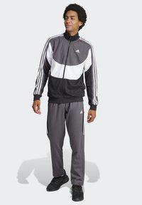 Completo sportivo nero e grigio con accenti bianchi, composto da una giacca con zip e pantaloni con vita elasticizzata. Maniche a righe, tessuto morbido.
