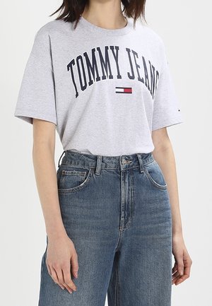 Camiseta de cuello redondo gris con "TOMMY JEANS" impreso en azul marino, combinada con jeans de mezclilla azul de tiro alto. Ajuste casual con mangas cortas.