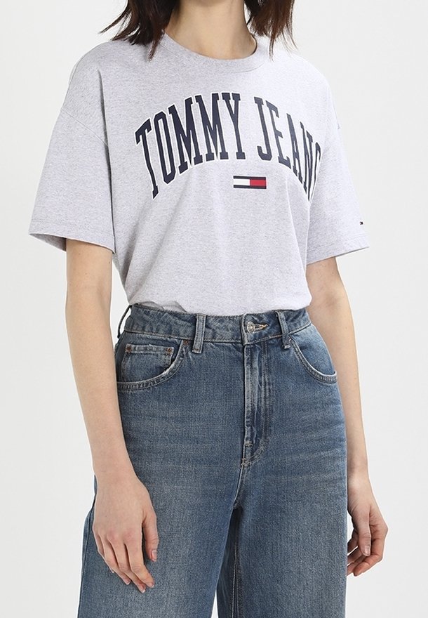 Camiseta de cuello redondo gris con "TOMMY JEANS" impreso en azul marino, combinada con jeans de mezclilla azul de tiro alto. Ajuste casual con mangas cortas.