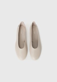 Ett par beige balletskor från Calvin Klein med runda tår, visade sida vid sida på en enkel vit bakgrund.