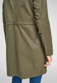 Olive green, lightweight, long-sleeve jacket with a cinched waist, straight cut, and minimal stitching details. Smooth, matte fabric texture.
