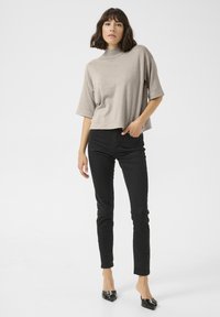 Top beige cropped avec un col montant et des manches courtes, associé à un jean slim noir et des escarpins noirs à bout pointu. Design et texture clairs.
