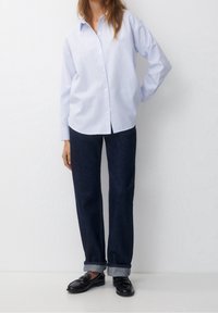 Lichtblauw en wit gestreepte button-up overhemd, relaxed fit, met lange mouwen. Gecombineerd met donkerblauwe opgerolde jeans en zwarte instappers.