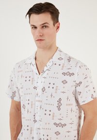 Witte T-shirt met korte mouwen met abstracte bruine en oranje geometrische patronen, voorzien van een knoopsluiting aan de voorkant en een relaxte kraagontwerp.