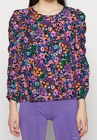 Blusa floreale con sfondo nero, decorata con fiori viola, arancioni e blu. Maniche a sbuffo arricciate e scollatura rotonda.