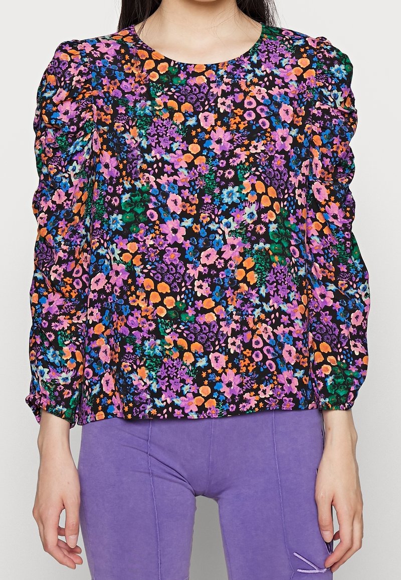 Blusa floreale con sfondo nero, decorata con fiori viola, arancioni e blu. Maniche a sbuffo arricciate e scollatura rotonda.
