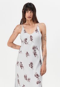 Ermeløs grå kjole med burgunderblomstertrykk, v-hals og tynne stropper. Stoffet er jevnt med en lett glans.