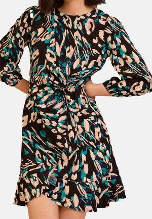 Femme portant une robe noire avec un imprimé floral abstrait beige et bleu sarcelle, manches longues bouffantes, un nœud à la taille et un ourlet à volants.