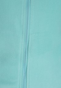 Giacca in fleece di un teal chiaro con una cerniera centrale. Texture morbida e finitura liscia, caratterizzata da cuciture sottili lungo la linea della cerniera.