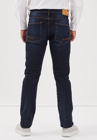 Granatowe dżinsy o prostym kroju, z tylnymi kieszeniami i jasnymi przeszyciami. Noszone z białymi trampkami.