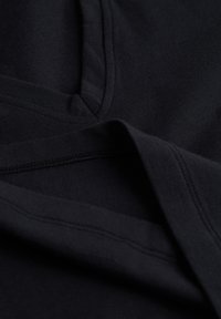 Czarna bawełniana tkanina o gładkiej fakturze, z dekoltem w serek i kontrastowym przeszyciem wzdłuż brzegów i szwów.