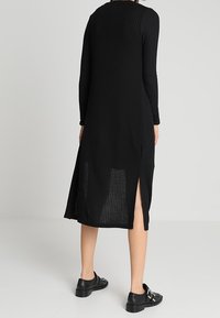 Black ribbed long-sleeve dress with side slits, made of lightweight fabric, featuring a rounded neckline and a fitted silhouette.