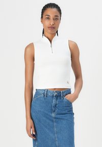 Vit ribbad crop top med hög krage och dragkedja fram, i kombination med en högmidjad blå denimkjol. Enkelt design och åtsittande passform.