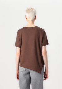 Brun kortermet t-skjorte med rund hals. Bak er det en asymmetrisk nederkant, kombinert med lys grå jeans. Enkelt mønster.
