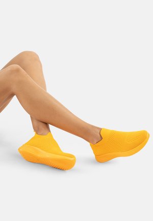 Yellow slip-on sneakers with a textured, breathable mesh upper and a thick, cushioned sole, featuring a flexible design and minimal detailing.