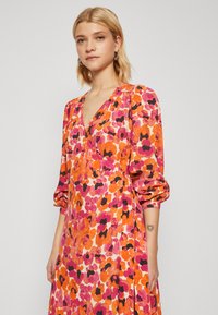 Blommönstrad klänning med livfulla nyanser av rosa, orange och svart, med djup V-ringning, puffärmar och en avslappnad silhuett.