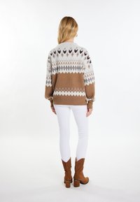 Knit pulover ima geometrijski vzorec v sivi, rjavi in krem barvi; ima oversize kroj z spuštenimi rameni, kombiniran z belimi oprijetimi hlačami in rjavimi škornji.