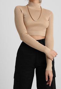 Top court à manches longues côtelé beige clair avec col roulé et coupe ajustée. Associé à un pantalon cargo noir taille haute, avec poches latérales.