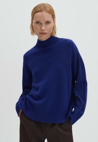 Pull à col montant bleu en maille douce, avec des manches amples et des poignets et ourlet côtelés, offrant une coupe décontractée.