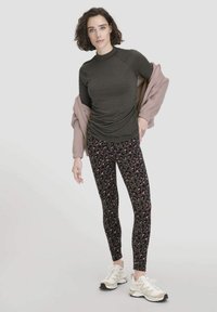 Donkergrijze lange mouwen top gecombineerd met zwarte leggings met een roze luipaardprint, aangevuld met een lichtroze jas en beige sneakers.