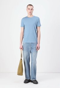 Γαλάζιο μπλουζάκι με λαιμόκοψη, ξεθωριασμένο μπλε τζιν με ίσια γραμμή και μαύρα παπούτσια. Μια μπεζ τσάντα κρατιέται από το ένα χέρι. Απλός σχεδιασμός.