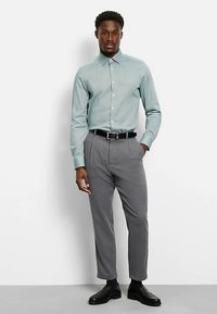 Light blue button-up shirt with a collar, paired with gray tapered trousers, and black shoes. Smooth fabric and tailored fit.