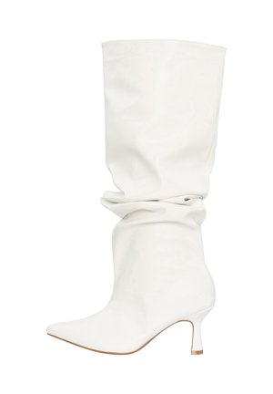 Hvid slasket læderstøvle til midtkalv med spids tå og lav, buet hæl, vist mod en ensfarvet hvid baggrund.