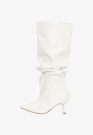 Botte blanche ample en cuir mi-mollet avec bout pointu et talon bas courbé, présentée sur un fond blanc uni.