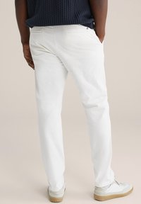 Hvide bomuldsbukser med lige pasform, baglommer og diskret syning; kombineret med lette sneakers i grå og creme farver.