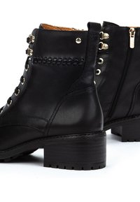 Black leather ankle boots with lace-up front, side zipper, decorative stitching, gold eyelets, and chunky low heel on white background.