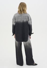 Camicia di jeans nera con una sfumatura dal scuro al chiaro; vestibilità ampia con polsini a bottone. Abbinata a pantaloni a gamba larga coordinati, anch'essi con sfumatura.