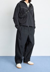 Svart lättviktsjacka med huva, dragkedjestängning, framfickor; tillsammans med lösa svarta byxor och vita sneakers med gummisålar.