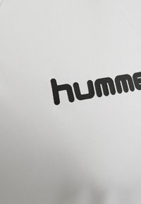 Zwarte tekst „hummel“ gedrukt op een wit stoffen oppervlak, dat een deel van een logo of merknaam toont.