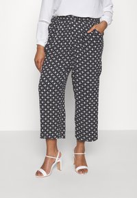 Zwart-wit gestreepte broek met een elastische tailleband, cropped lengte, zijzakken en een relaxte pasvorm. Gecombineerd met witte haksandalen.