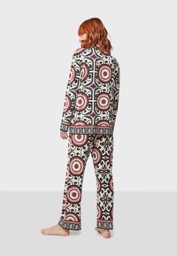 Conjunto de pijama estampado en color crema, con motivos circulares en rojo y negro. Camiseta de manga larga y pantalones con ribetes en contraste y tejido suave.