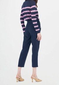 Pantalon bleu marine fuselé associé à un haut à manches longues rayé bleu marine et rose. Les chaussures sont beige avec un petit talon et une bride arrière.