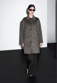 Cappotto a stampa leopardata nelle tonalità di grigio, con chiusura frontale a bottoni e colletto, abbinato a pantaloni neri eleganti e tacchi appuntiti.