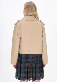 Beige cropped jakke med skjortekrave, knapdetaljer og lange ærmer, parret med en mørkternet lagdelt nederdel.