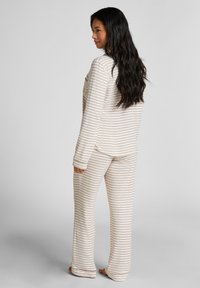 Gestreept pyjama-set met een crèmekleurige basis en dunne bruine strepen. Zachte stof, lange mouwen en loszittende broek met elastische taille.