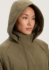 Vaatteet vuorattu huppu takki oliivi vihreä, jossa on pehmeä teksturoitu vuori, korkea kaulus ja timantin muotoinen ompelu.
