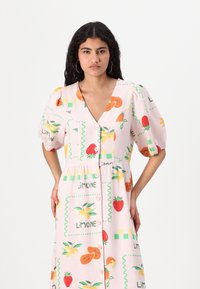 Ροζ φόρεμα με σχέδιο φρούτων που έχει πορτοκάλια, φράουλες και πράσινα στοιχεία. Με φουσκωτά μανίκια, V-λαιμόκοψη και μπροστινό κλείσιμο με κουμπιά.