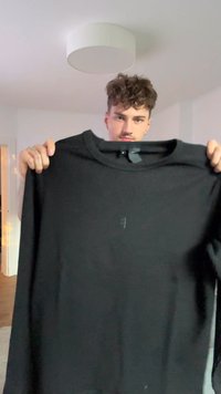 Camisa preta de manga longa com decote redondo, apresentando uma construção de costura plana e uma textura subtil. Etiqueta visível no decote.