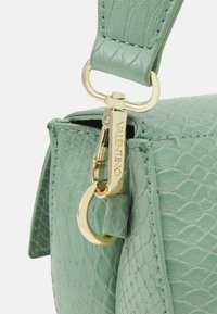 Sac en cuir vert texturé avec une attache métallique dorée et des éléments en métal, doté d'une fermeture éclair bien visible et de détails de couture soignés.