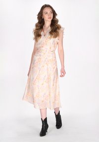 Blumenkleid in sanften Pastellfarben mit Rüschensäumen, taillierter Taille und fließender Silhouette. Kombiniert mit schwarzen Knöchelstiefeln.
