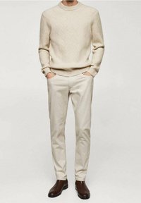Maglione beige lavorato a maglia con un motivo testurizzato, abbinato a pantaloni beige chiaro e stivaletti marroni alla caviglia. Silhouette semplice e raffinata.